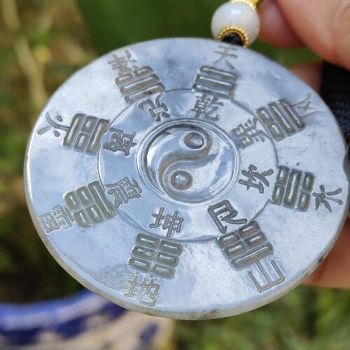 a hand holding a necklace with a yin yang symbol