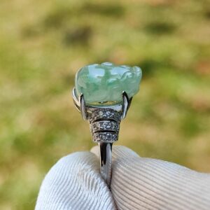 a hand holding a ring with a jade stone
