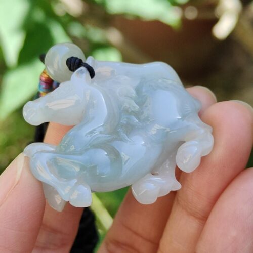 a hand holding a jade horse pendant