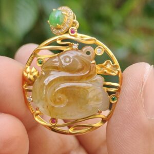 a hand holding a gold pendant with a green and red stone in it