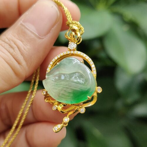 a hand holding a gold necklace with a green stone and diamonds