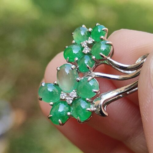 a hand holding a ring with green stones