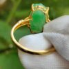 a hand holding a gold ring with a green stone