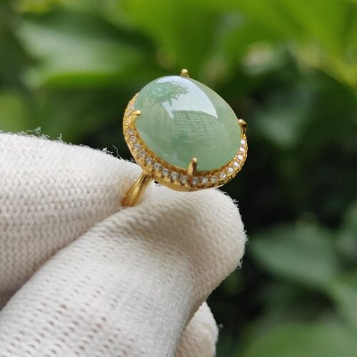 a hand wearing a white glove holding a ring with a green stone