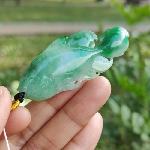 a hand holding a jade fish pendant