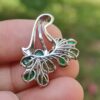 a hand holding a silver and green earring