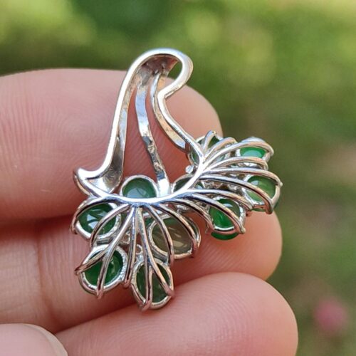 a hand holding a silver and green earring