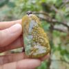 a hand holding a green and yellow stone pendant