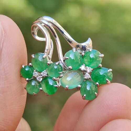 a hand holding a silver ring with green stones