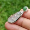 a hand holding a silver and green pendant