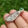 a hand holding a silver pendant with a green stone
