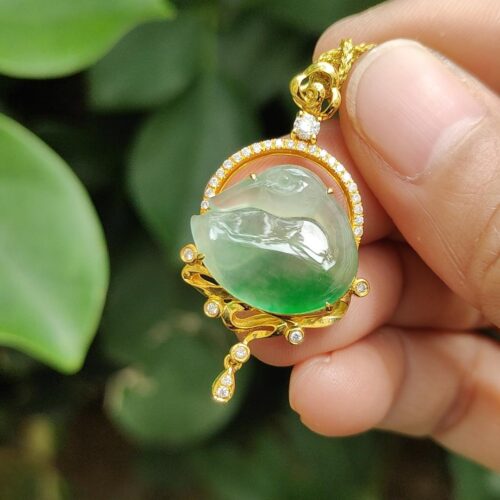 a hand holding a gold pendant with a jade stone in the center