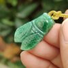 a hand holding a green stone insect pendant