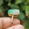a hand holding a gold ring with a jade stone on it