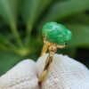 a hand holding a gold ring with a jade stone on it
