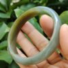 a hand holding a round green bracelet