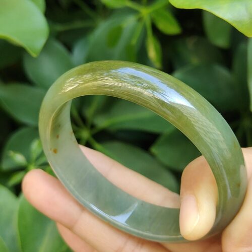 a hand holding a round green bracelet