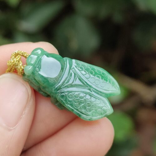 a hand holding a green insect pendant