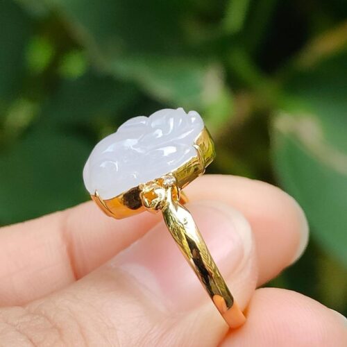 a hand holding a gold ring with a carved white stone