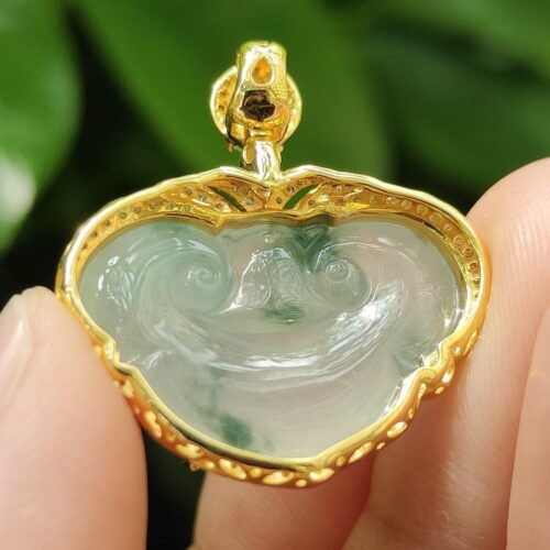 a hand holding a gold and green pendant