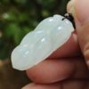 a hand holding a white jade leaf pendant