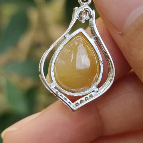 a hand holding a silver and yellow stone pendant