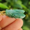 a hand holding a green stone pendant - Cicada