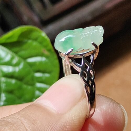 a finger holding a ring with a jade stone on it