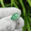a hand wearing a gloved hand holding a ring with a green stone