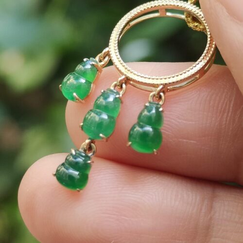 a hand holding a gold ring with green stones